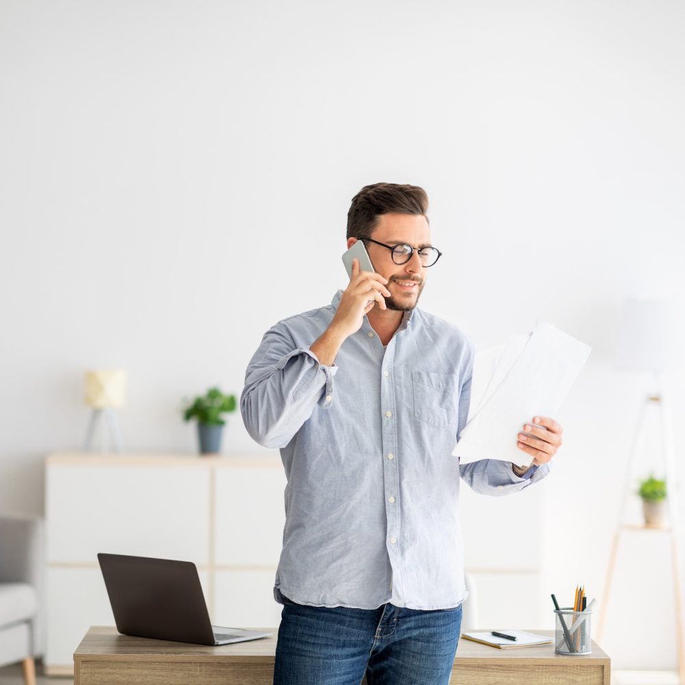 Home office concept. Confident millennial entrepreneur talking on cellphone and discussing financial